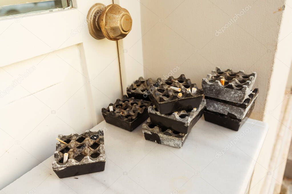 Ashtrays with cigarette butts on a white table. Dirty ashtrays in the shape of a square. A pile of used ashtrays in a cafe