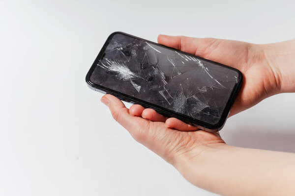 Смартфон со сломанным экраном в руке женщины на белом фоне. Crash защитного закаленного стекла для смартфона. Дорогой смартфон со сломанным экраном