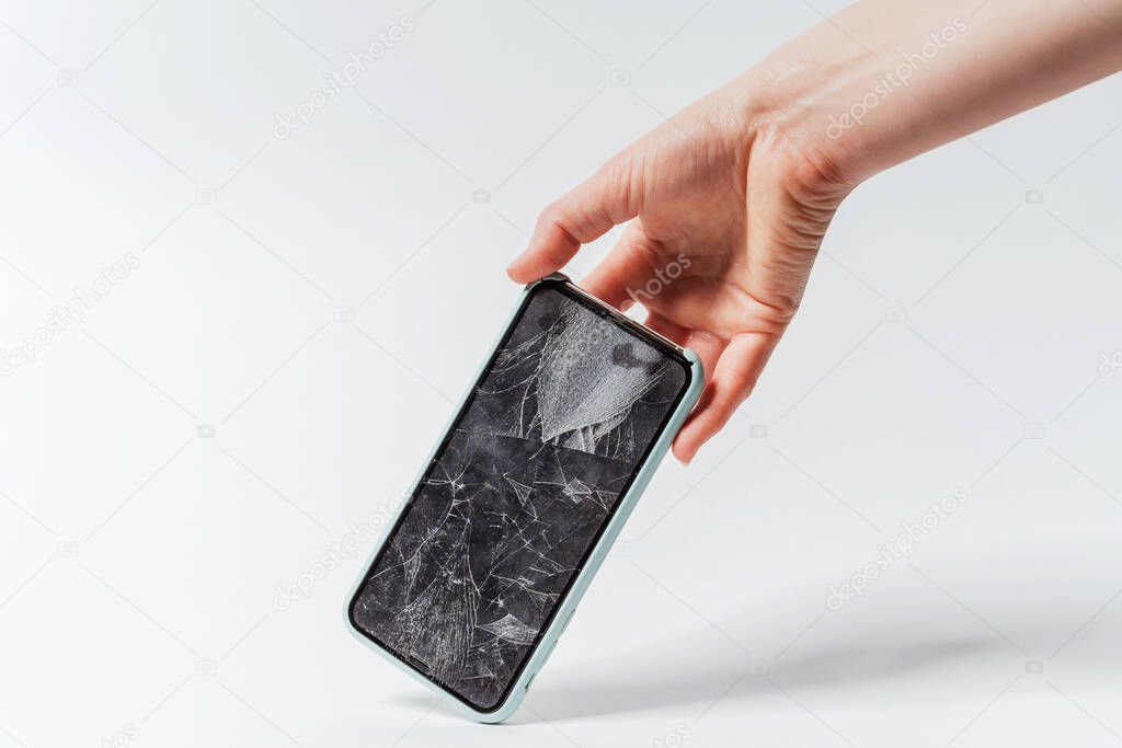 A smartphone with a broken screen in a woman's hand on a white background. Crash protective tempered glass for smartphone. Expensive smartphone with a broken screen