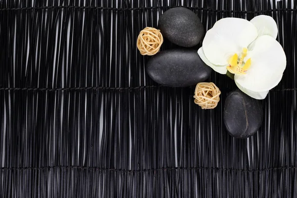Orquídea com pedras zen e bolas de vime no fundo preto — Fotografia de Stock