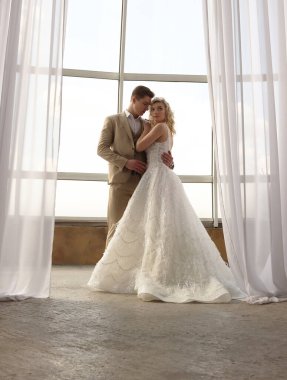 Yeni evliler büyük panoramik pencerenin arkasında duruyor. Romantik çift gelin ve damat