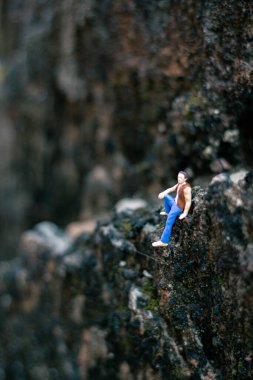 Minyatür insanlar, genç adam doğal ışıkla bir kayanın üzerinde oturuyor.