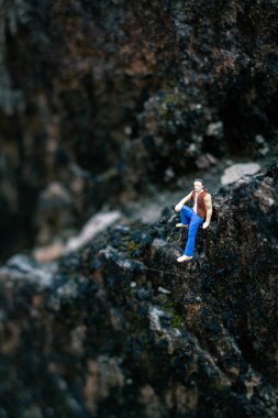 Minyatür insanlar, genç adam doğal ışıkla bir kayanın üzerinde oturuyor.