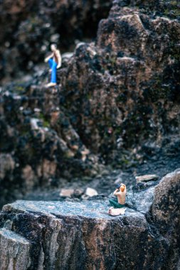 Minyatür insanlar, genç adam doğal ışıkla bir kayanın üzerinde oturuyor.