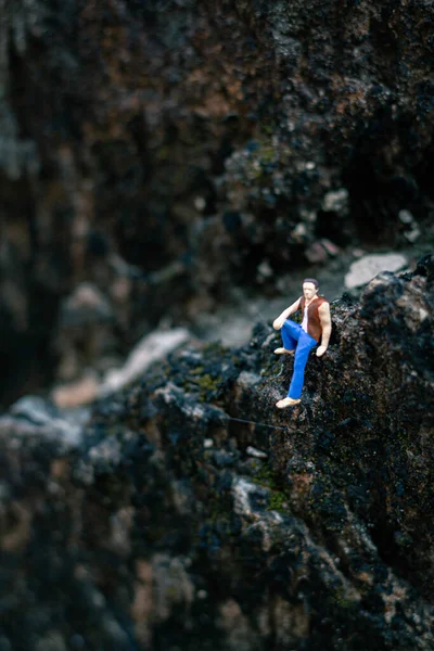 Minyatür insanlar, genç adam doğal ışıkla bir kayanın üzerinde oturuyor.