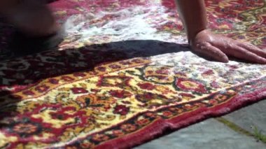 Bir kadın evin avlusunda, caddede kirli bir halıyı fırçalıyor. Temiz suyla çalkala. Tozdan çok köpük çıkıyor. Kapalı yıkama halısı. Fırça halıyı temizler