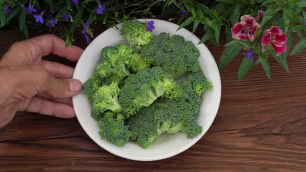 Brócolis vegetal em uma placa branca em um fundo de madeira escuro emoldurado com flores naturais — Vídeo de Stock