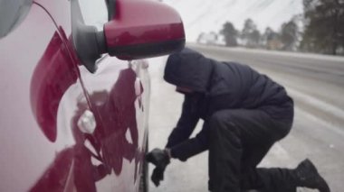 Adamın biri arabanın tekerleğini değiştiriyor. Bulutlu bir kış gününde yol kenarında acil bir araba durağı.