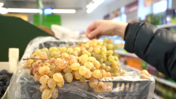 Ruka ženy v nepromokavé bundě vybírá hrozny v supermarketu. — Stock video