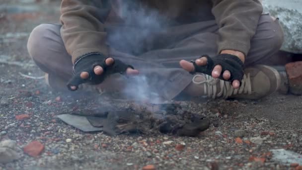 Ein Obdachloser wärmt sich am Feuer die Hände. Szene nach der Apokalypse. Hände in schwarzen zerrissenen Handschuhen. Nahaufnahme. Schwache Wärme von einem kleinen Feuer — Stockvideo