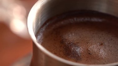 Çelik bir Türk 'te öğütülmüş sade kahve pişirilir ve ocakta kaynatılır. Yüzeyde köpük var. Yakın çekim.