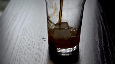 Buzlu bir bardağa kola dök. Soğuk, ferahlatıcı kola hafif arka planda buzlu bir bardağa dökülür. Pencereden gelen doğal gün ışığı. Yavaş çekim