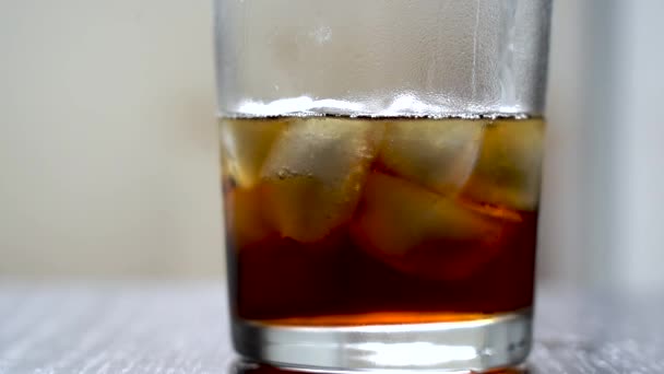 Dark drink in a glass with ice on the table. Cold refreshing cola in a glass with ice on a white background. Natural daylight. Ice cold drink made from a cool caffeinated drink. — Stock Video