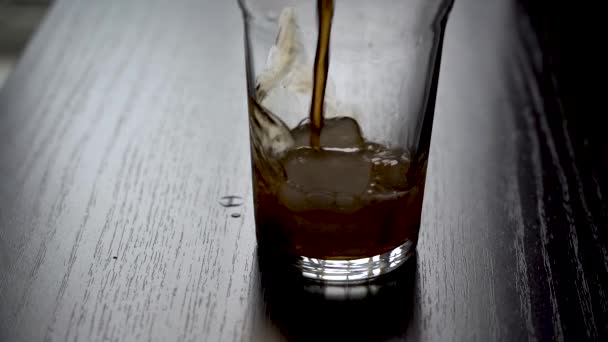 Vierta la cola en un vaso con hielo. La cola refrescante fría se vierte en un vaso con hielo sobre un fondo claro. Luz natural del día desde la ventana. Movimiento lento — Vídeos de Stock