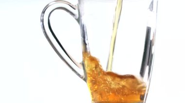 Şeffaf bir bardağı lezzetli bir içecekle doldur. İçki beyaz arka planda şeffaf bir çay bardağına dökülüyor.