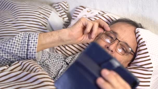 Älterer Mann im Bett mit Smartphone. Fernkommunikation mit Familie und Freunden über das Internet — Stockvideo