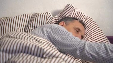 Yataktaki yaşlı adam uyumak için ışığı kapatıyor.