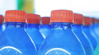 Vitrinin yanındaki dükkanda bir sürü plastik içki şişesi var. Yakından çek. Karbonatlı meşrubat şişeleri.