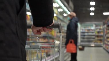 Süper Market 'te seçilmiş ürünler var. Yavaş bir hareket yap. Dükkanda hareket eden boş bir el arabasının yanında. İnsan eli. Yakın plan.