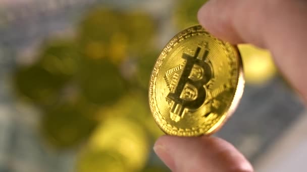 Håll en guldmynt mynt mynt på en suddig bakgrund av många guldmynt. Fingrarna på en man som håller i Bitcoin, Guldmynt — Stockvideo