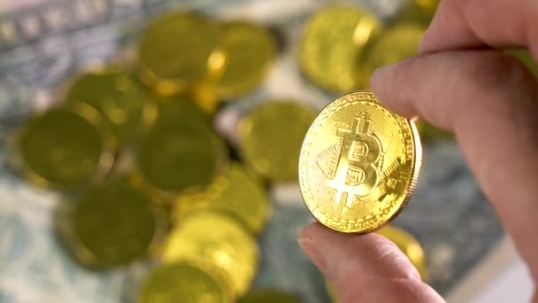 Przytrzymaj złotą monetę Bitcoin na rozmytym tle wielu złotych monet. Palce człowieka gospodarstwa Bitcoin, złota moneta — Wideo stockowe