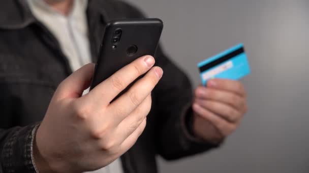 ジャケットの認識できない男はスマートフォンとプラスチック製の銀行カードを持っています。クレジットカードや携帯電話で手を閉じる｜オンライン銀行 — ストック動画