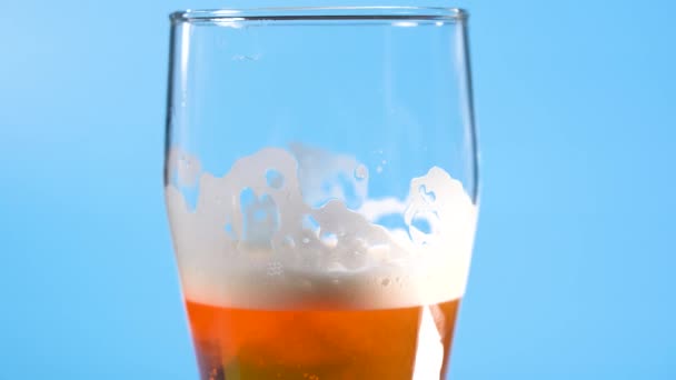 Licht bierschuim in een glas op een lichtblauwe achtergrond — Stockvideo