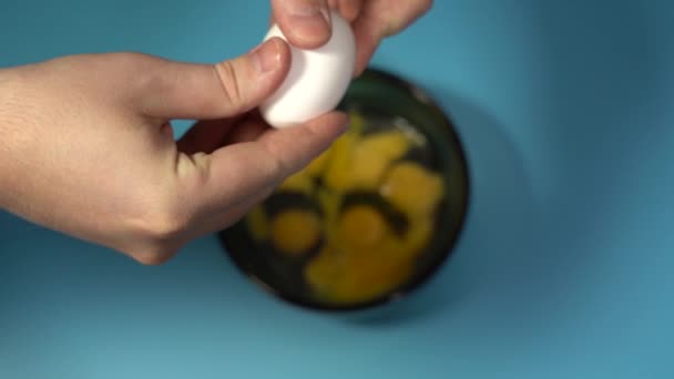 A férfi kezek egy repedt tojást tartanak. Törd össze a tojást a kupán. Kék háttér. Lassú mozgás — Stock videók