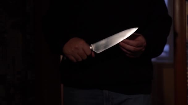 Um homem se aproxima no escuro, segurando uma grande faca em suas mãos. — Vídeo de Stock