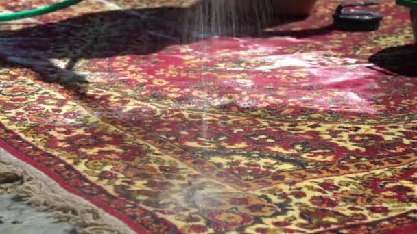 Enjuague la alfombra con agua limpia usando una manguera. Lave las alfombras con espuma y agua afuera en un día soleado cálido. Primer plano — Vídeos de Stock