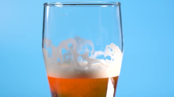 Licht bierschuim in een glas op een lichtblauwe achtergrond — Stockvideo