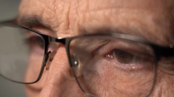 Крупный план Вид фокусированного пожилого человека в компьютерных очках, чтобы уменьшить напряжение глаз, чтение в Интернете до позднего вечера — стоковое видео