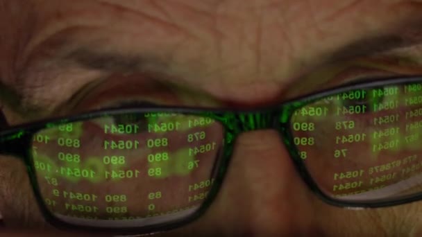 El programador con anteojos delante de la pantalla. Reflejo del monitor con un código numérico. — Vídeos de Stock