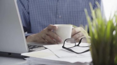 Adam kahve içer, Ofis Masası 'ndaki belgelerle çalışmayı durdurur.