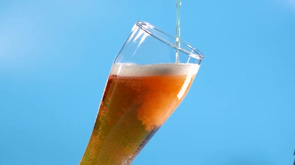 Cerveja Light é derramada em um copo inclinado em um fundo azul. Movimento Lento. Estúdio — Vídeo de Stock