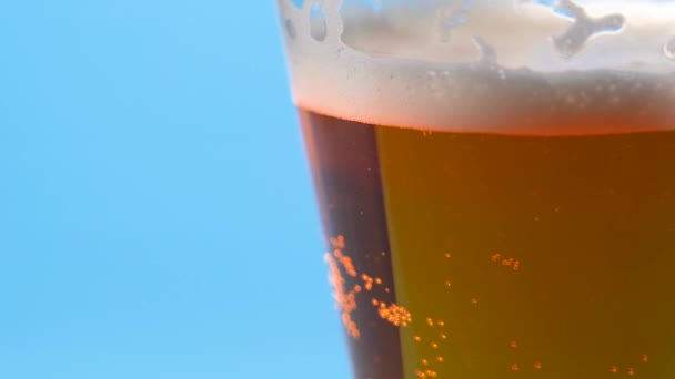 Licht bierschuim in een glas op een lichtblauwe achtergrond — Stockvideo