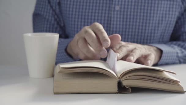 Die Hände des älteren Herrn schließen vorsichtig das dicke Buch und heben den Becher auf. Lesen Sie ein literarisches Buch zu Ende — Stockvideo