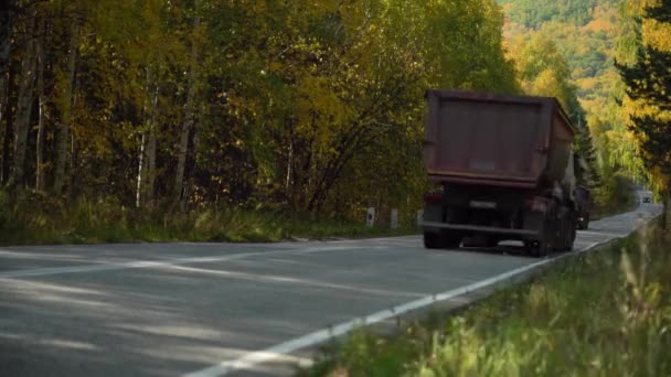 Les camions lourds à benne basculante roulent dans une région montagneuse boisée sur une route asphaltée par une journée ensoleillée d'automne — Video