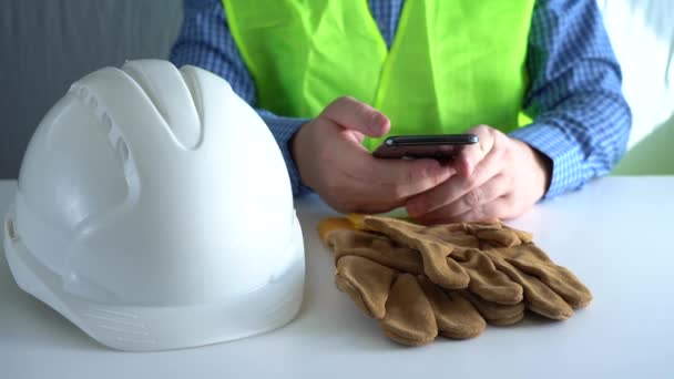 Il lavoratore edile legge i messaggi e utilizza uno smartphone mentre siede al tavolo — Video Stock
