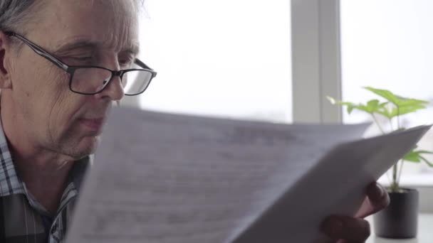 Un homme âgé avec des lunettes lit attentivement le document sur les feuilles — Video