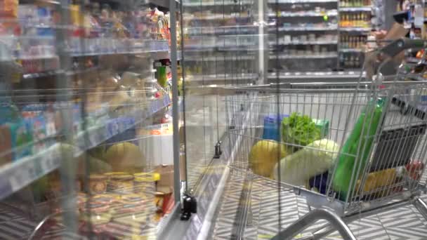 Bevásárlókocsi élelmiszerekkel Hűtőszekrények mellett. A hűtő üvegajtója becsapódott. — Stock videók