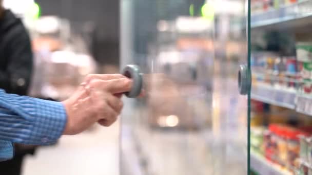 Oude man in de supermarkt. Een Shopper Opent de Koelkast in de Store. Oudere man selecteert voedsel in de supermarkt koelkast — Stockvideo