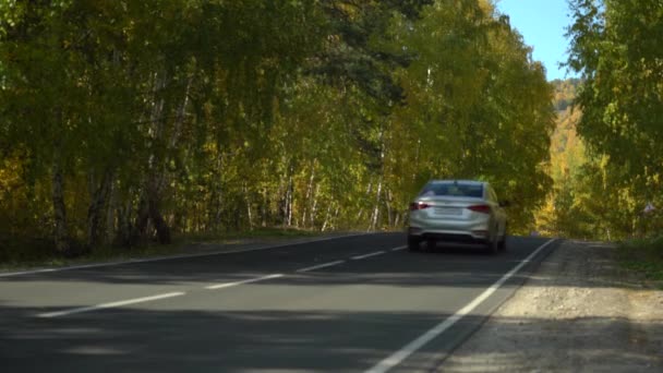 O carro passa rapidamente e se esconde atrás de uma colina entre árvores altas. Uma viagem de carro para fora da cidade em um dia ensolarado de outono. Paisagem montesa. Folhas amarelas nas árvores — Vídeo de Stock