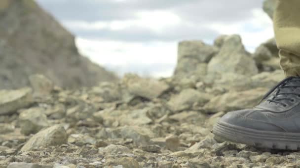 Mannelijke voeten in wandelschoenen en kaki broeken die over een bergpad lopen. Wandelen op de rotsen — Stockvideo
