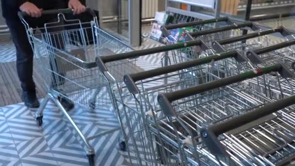 Close-up van een winkelend mannetje die een lege kruidenierswagen in een supermarkt of kruidenier opstelt — Stockvideo
