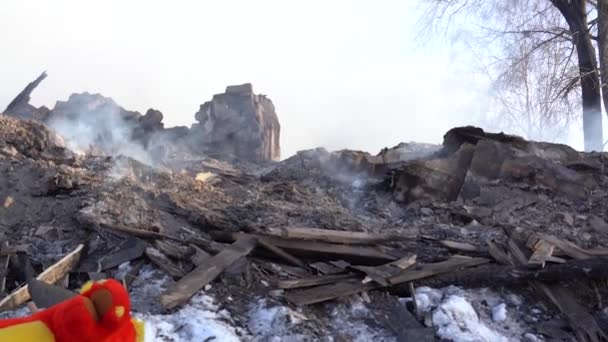 Una casa de madera se quemó. Fumar fragmentos carbonizados de construcción y juguetes suaves para niños en la nieve — Vídeos de Stock
