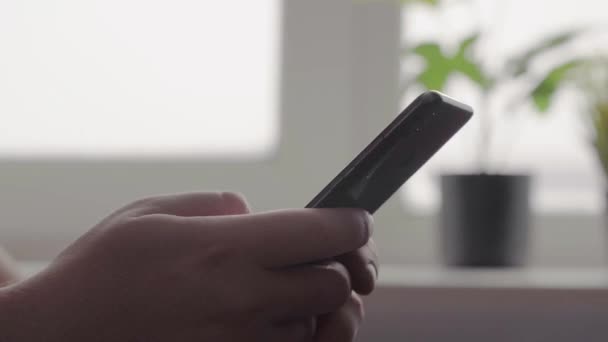 Un hombre sentado en la cocina mira a través de mensajes en un teléfono inteligente — Vídeos de Stock