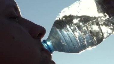 Ağır çekim. Bir adam şeffaf bir plastik şişeden Mavi Gökyüzüne karşı su içiyor. Yakın plan.