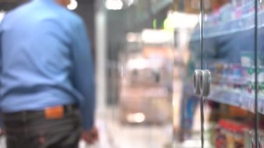 Süpermarketteki yaşlı adamın bulanık arkaplanı. Dükkanda buzdolabı açan bir müşteri var. Yaşlı adam marketten yiyecek seçiyor.