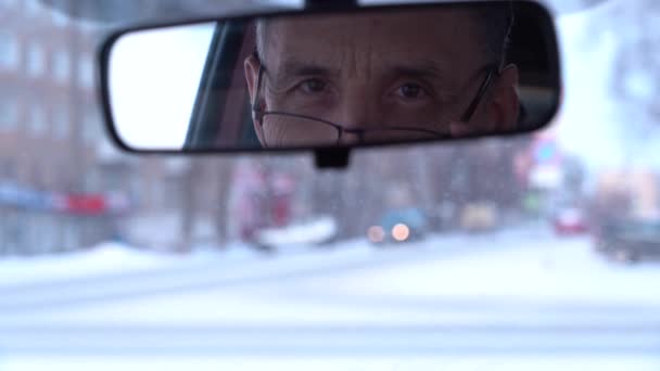 En äldre godmodig man med glasögon tittar i backspegeln, sitter i bilen — Stockvideo